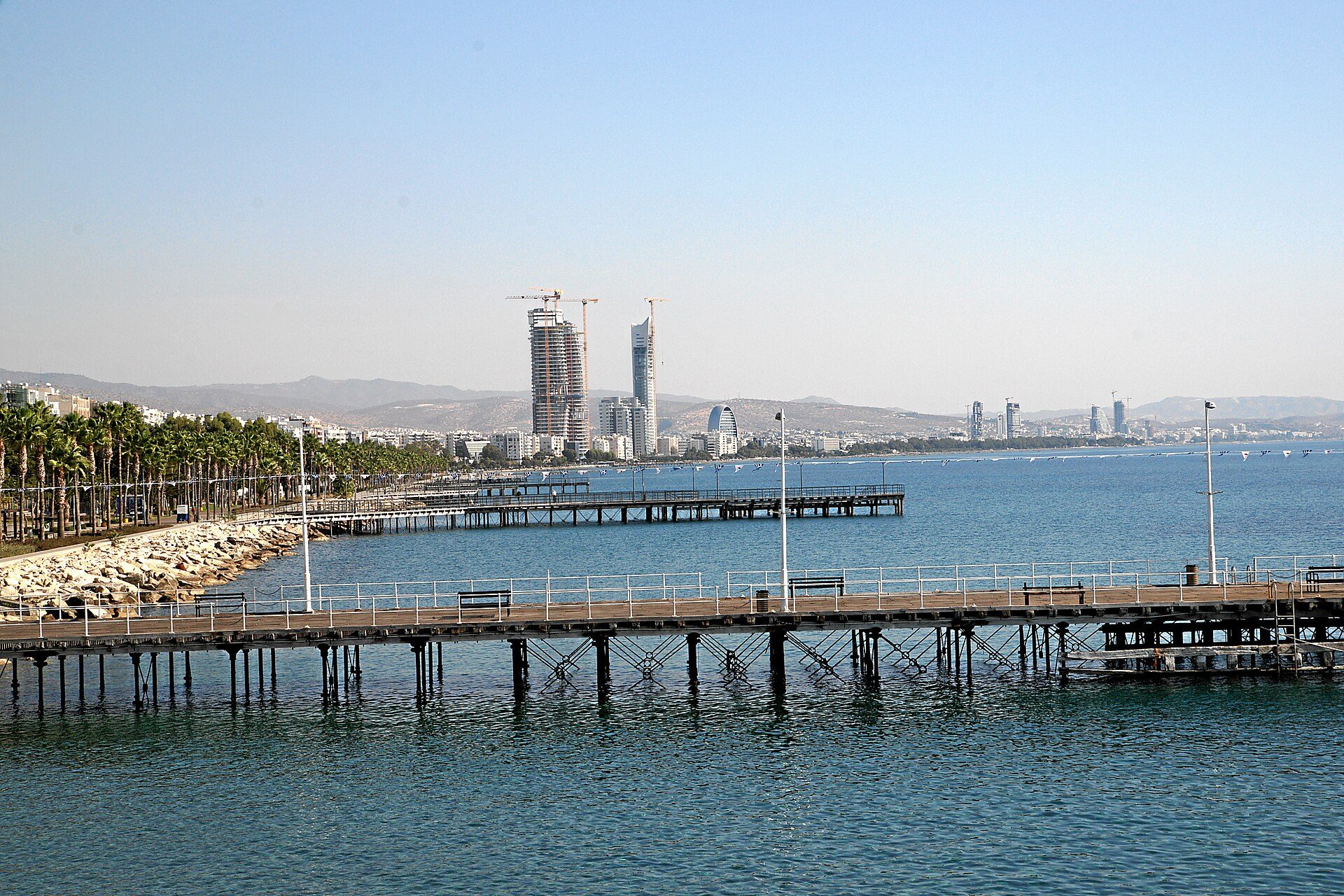 Ξύλινη προβλήτα που μπαίνει σε ήρεμη θάλασσα με πόλη στο βάθος